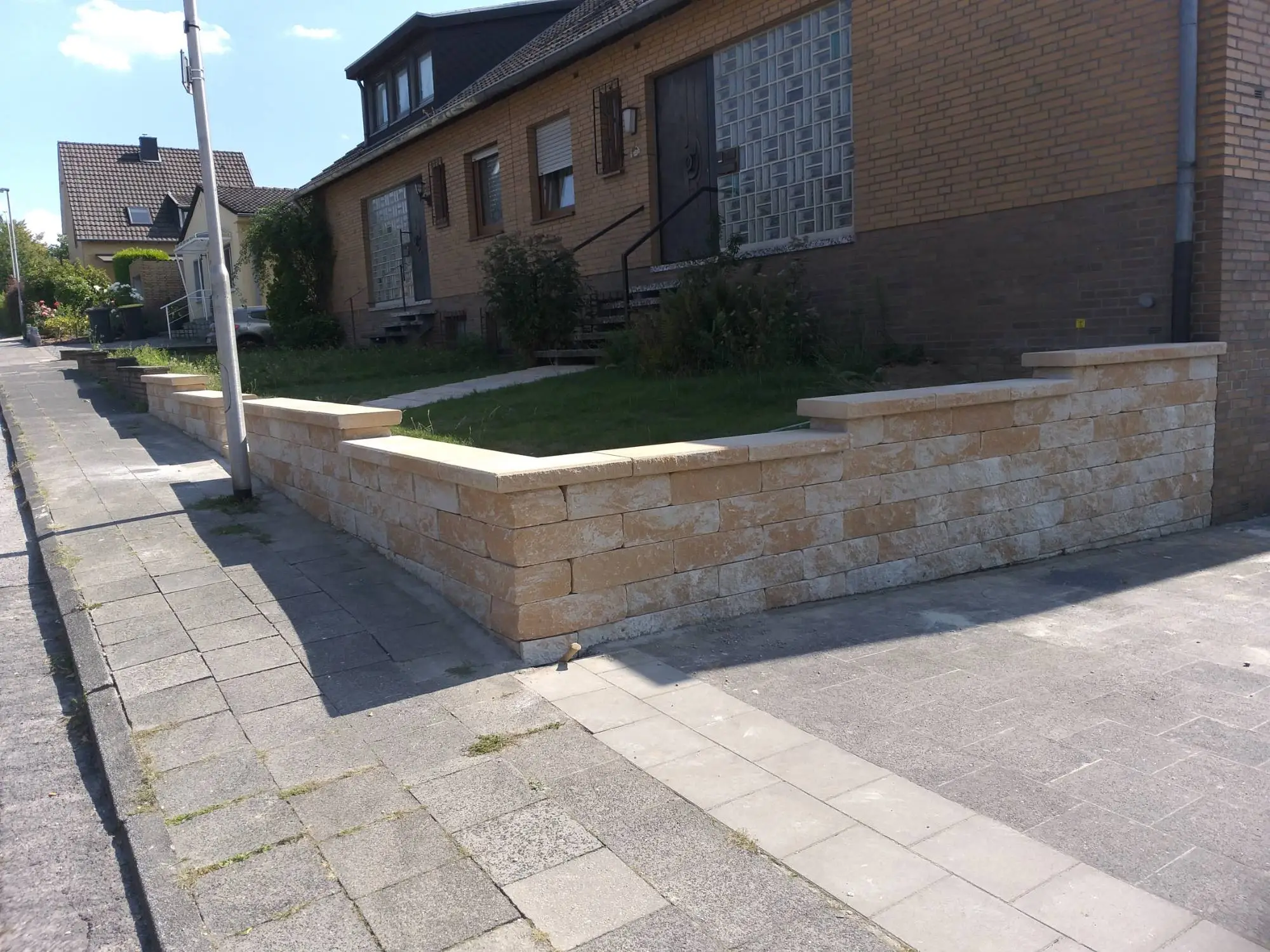 Neue Mauer aus hellem Naturstein mit Abdeckplatten um einen Vorgarten